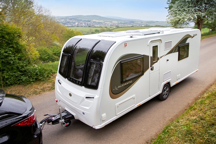 A black car towing a white caravan along a scenic route through classic British countryside.