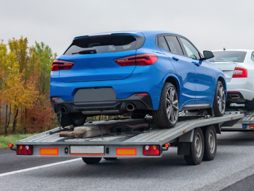 Blue car loaded on an open car trailer being transported.