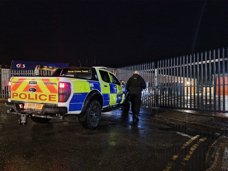 Police vehicle parked with an officer approaching locked gates at night.