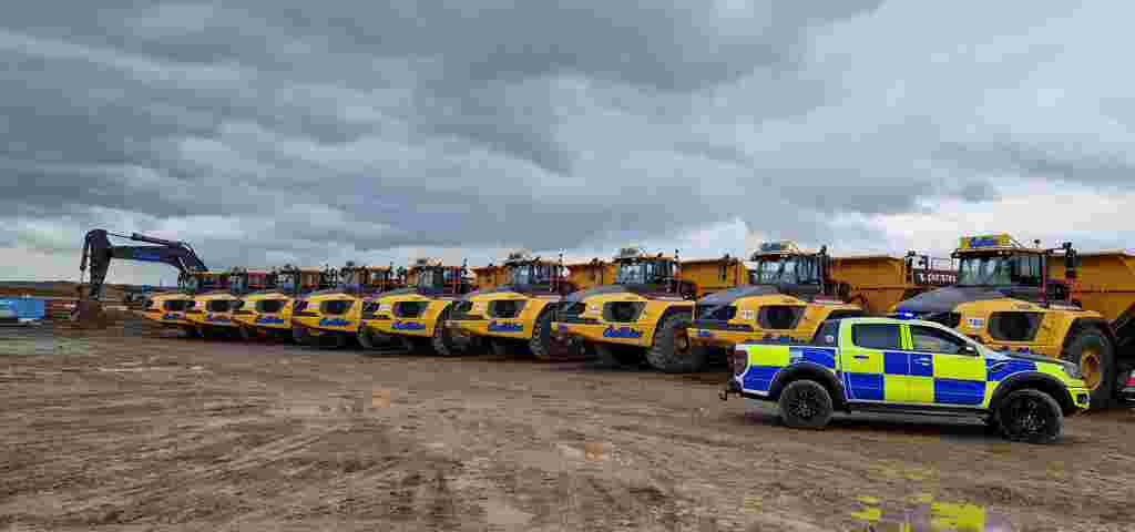 A police car parked to the right of a line of yellow off-road dumpers on a construction site.