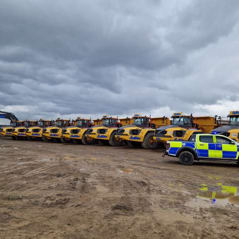 A police car parked to the right of a line of yellow off-road dumpers on a construction site.