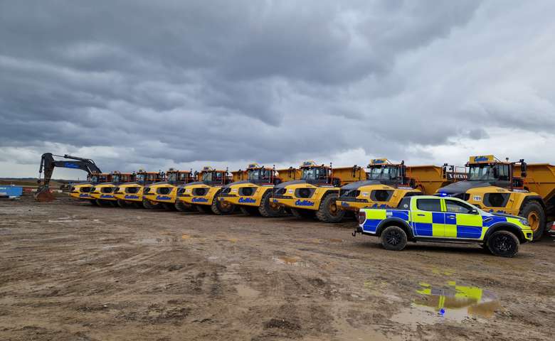 A police car parked to the right of a line of yellow off-road dumpers on a construction site.