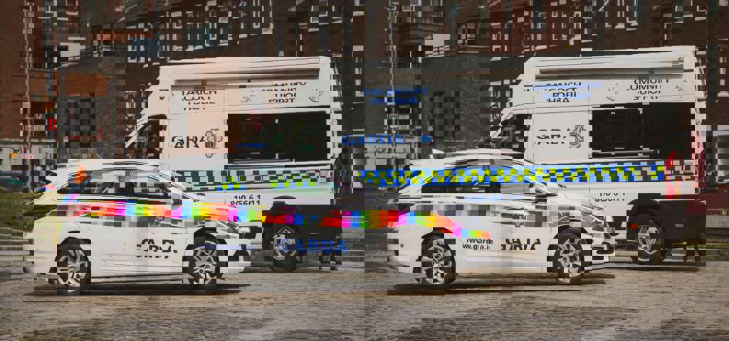 Rainbow flag-branded Garda car and a Garda community support van parked on a cobblestone street.