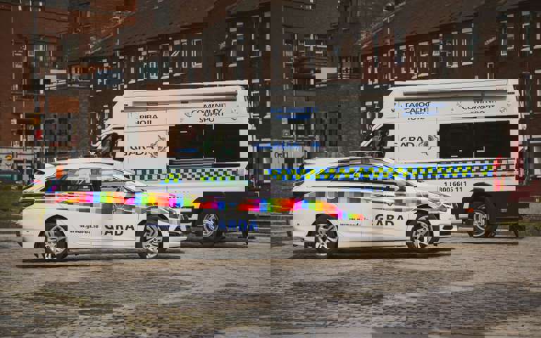 Rainbow flag-branded Garda car and a Garda community support van parked on a cobblestone street.