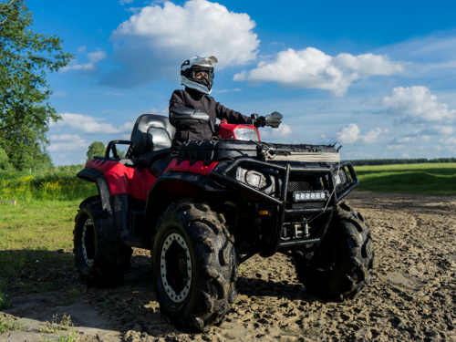 Rider stationary on a red quad bike in the countryside with green fields in the background.