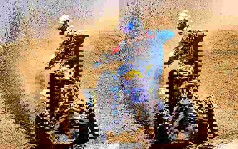 A rider on a sports ATV speeding down a sand dune, kicking up sand into the air.