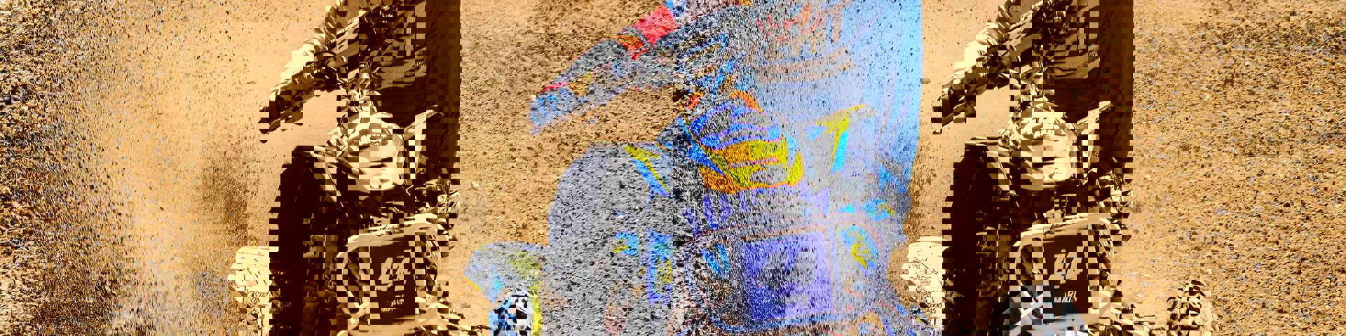 A rider on a sports ATV speeding down a sand dune, kicking up sand into the air.