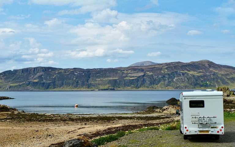 Motorhome parked beside a tranquil lake in a scenic setting.