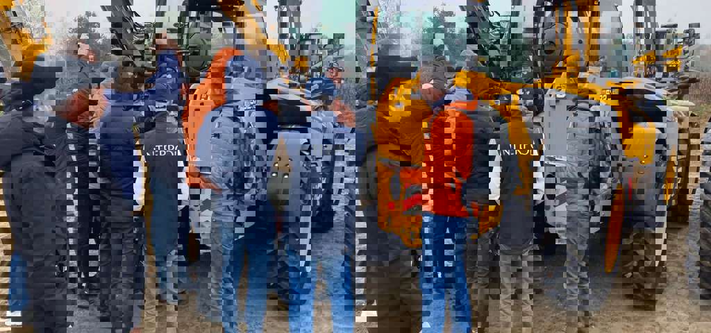 A group of students engaged in training, with JCBs and a rural landscape in the background.