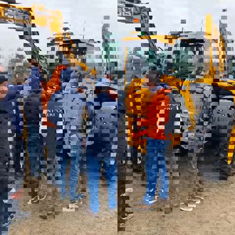 A group of students engaged in training, with JCBs and a rural landscape in the background.