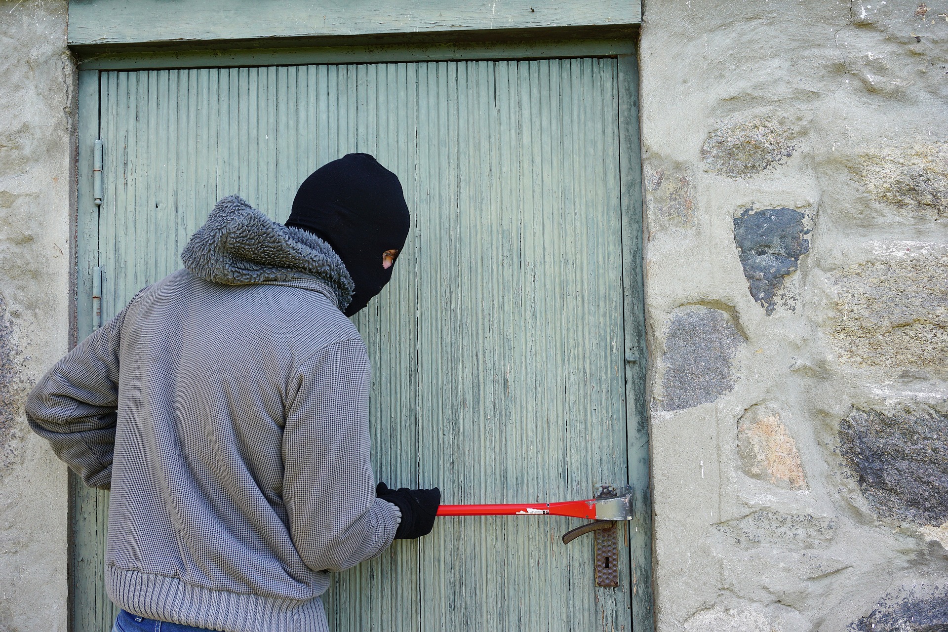A balaclava-clad burglar is attempting to force entry into a storage facility.