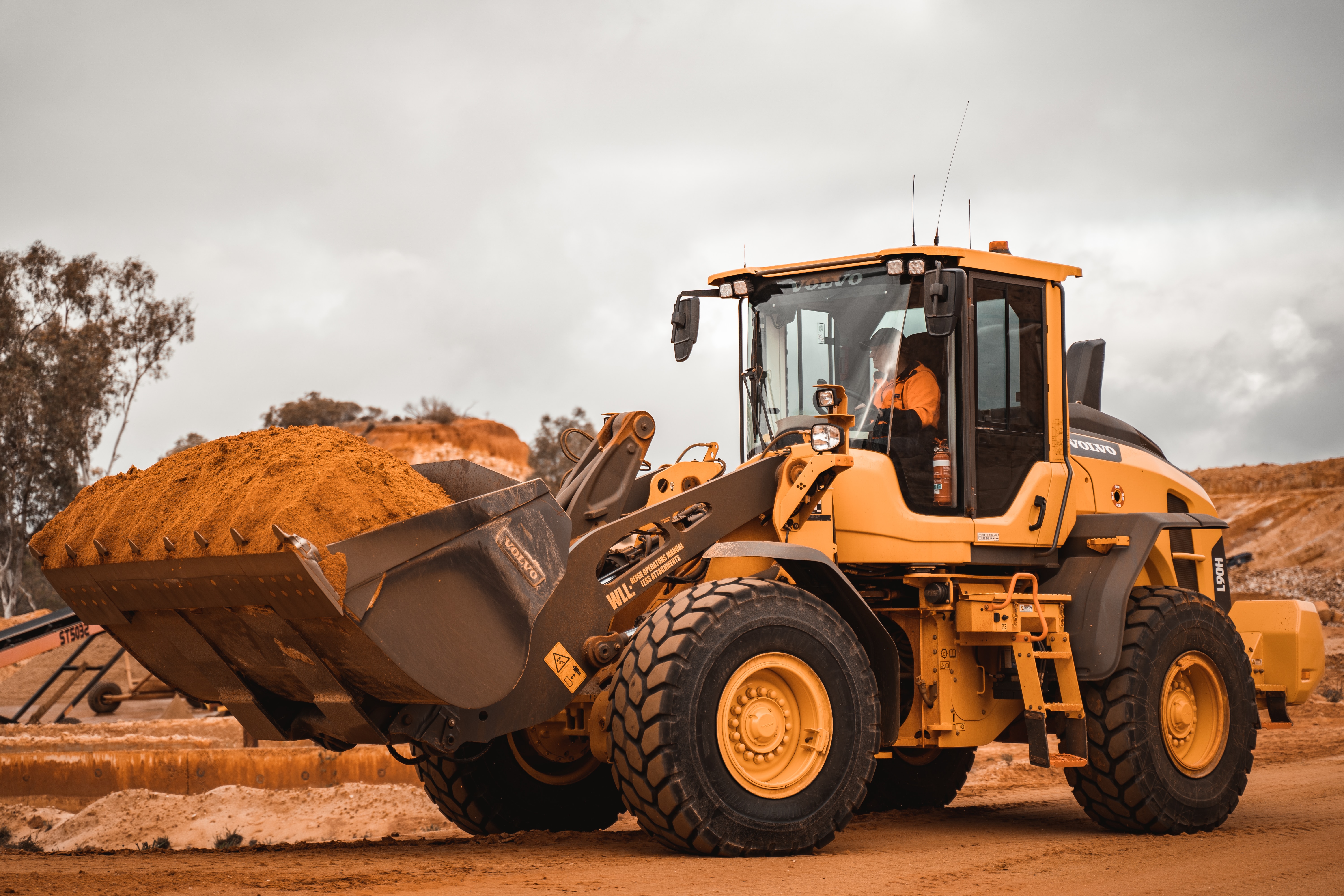 Yellow construction loader carrying a full bucket of material on a work site.