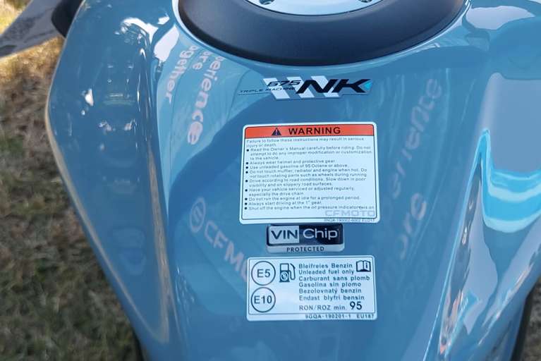 Close-up of a light blue CFMOTO motorcycle fuel tank featuring a VIN Chip domed resin warning label to indicate security protection.
