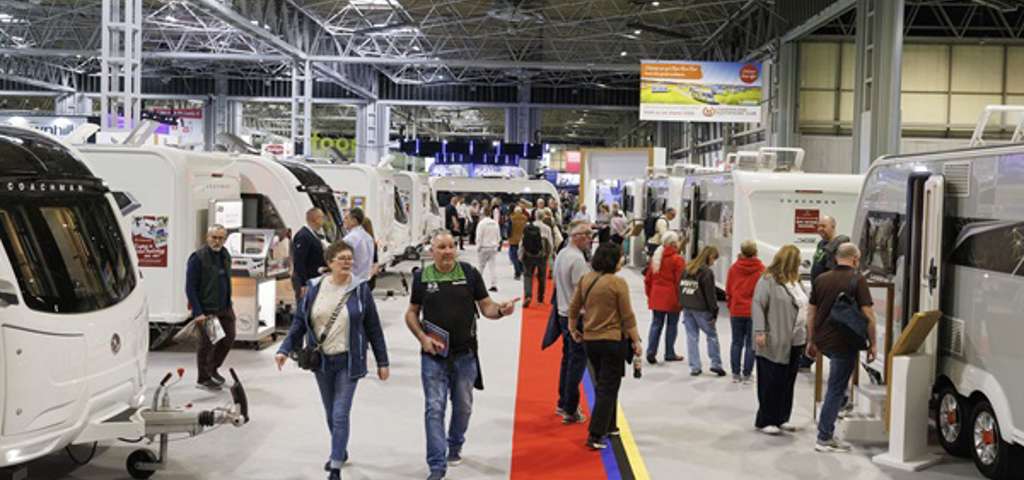 Visitors walking along a red-carpeted aisle at the Motorhome & Caravan Show, with caravans and motorhomes on either side