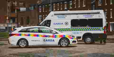 Rainbow flag-branded Garda car and a Garda community support van parked on a cobblestone street.