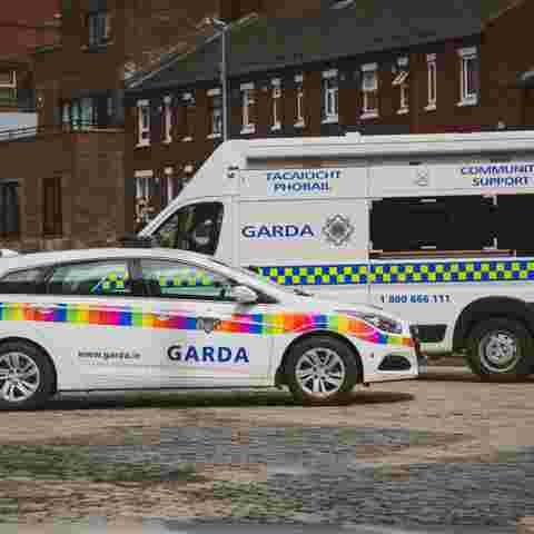 Rainbow flag-branded Garda car and a Garda community support van parked on a cobblestone street.