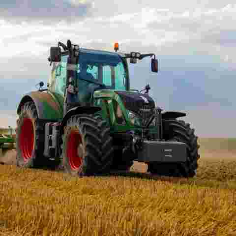 A green tractor is actively harvesting crops in a sunlit field.