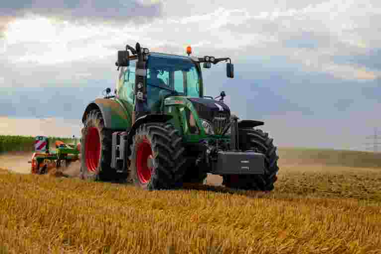 A green tractor is actively harvesting crops in a sunlit field.