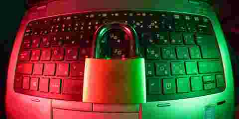 A black keyboard illuminated in pink and green light, with a padlock resting in the centre, symbolising cybersecurity.